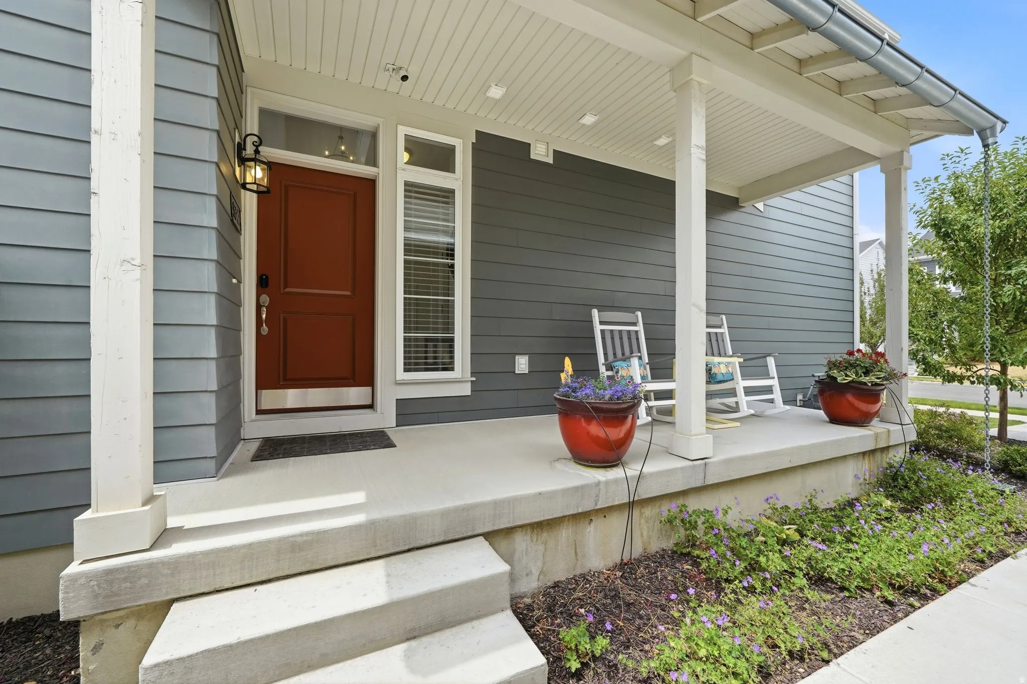 Inviting covered front porch with concrete steps, wood-finish columns, and a rich red entry door