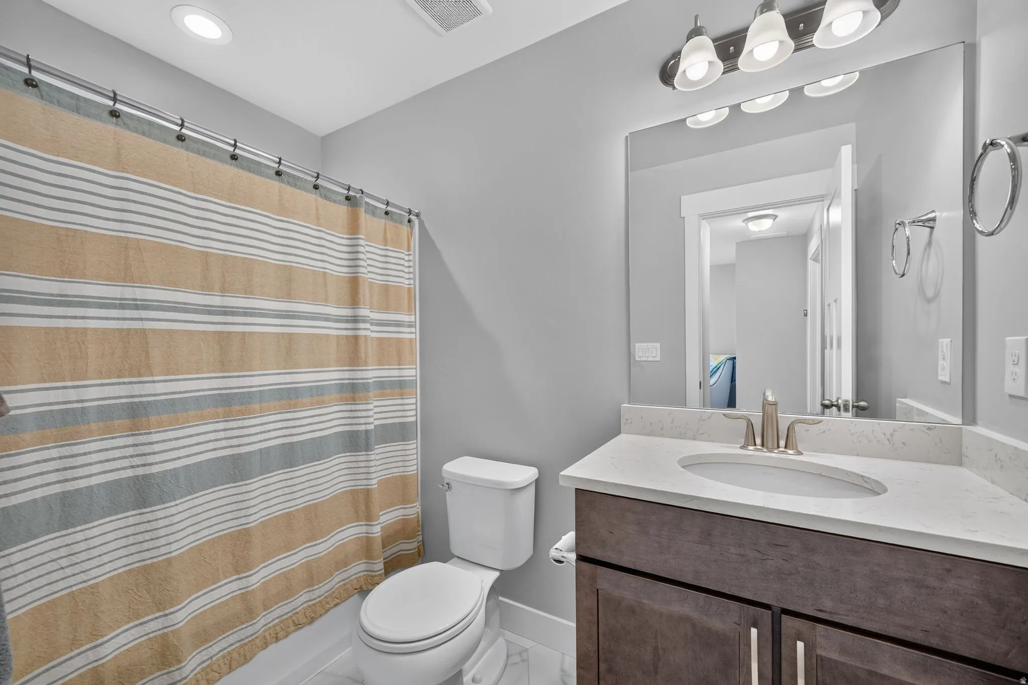 Full bathroom featuring a single vanity with a light-colored countertop and undermount sink, brushed nickel faucet, and wood-finish cabinetry