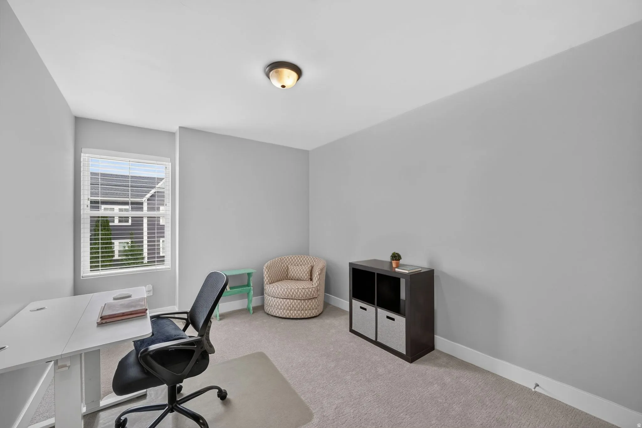 Versatile room featuring a single window with blinds, carpeted flooring, and neutral gray walls