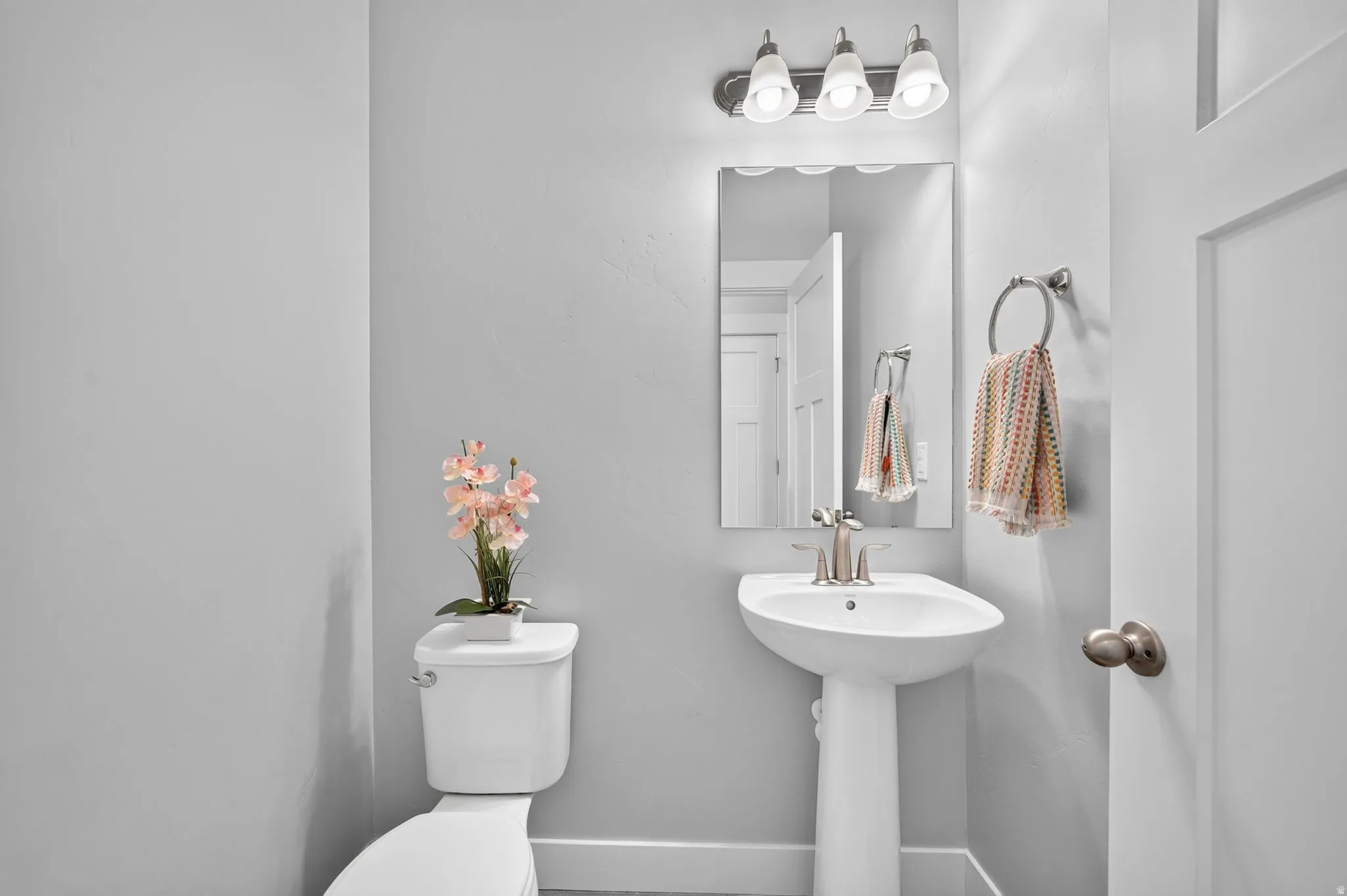 Modern powder room featuring a white pedestal sink, brushed nickel faucet, and a wall-mounted rectangular mirror