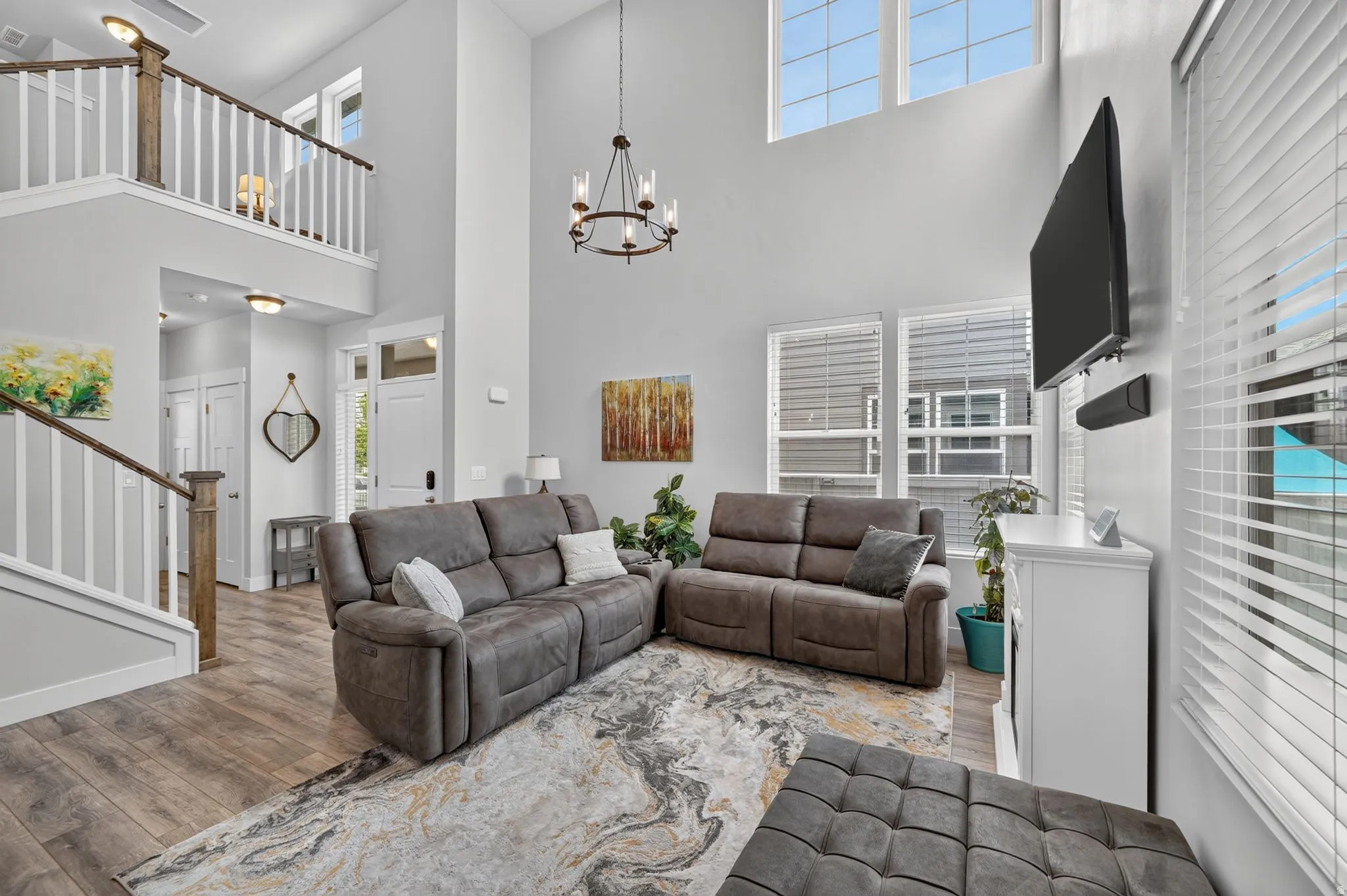 Two-story living area featuring wood-finish flooring, a contemporary chandelier, and large windows with blinds