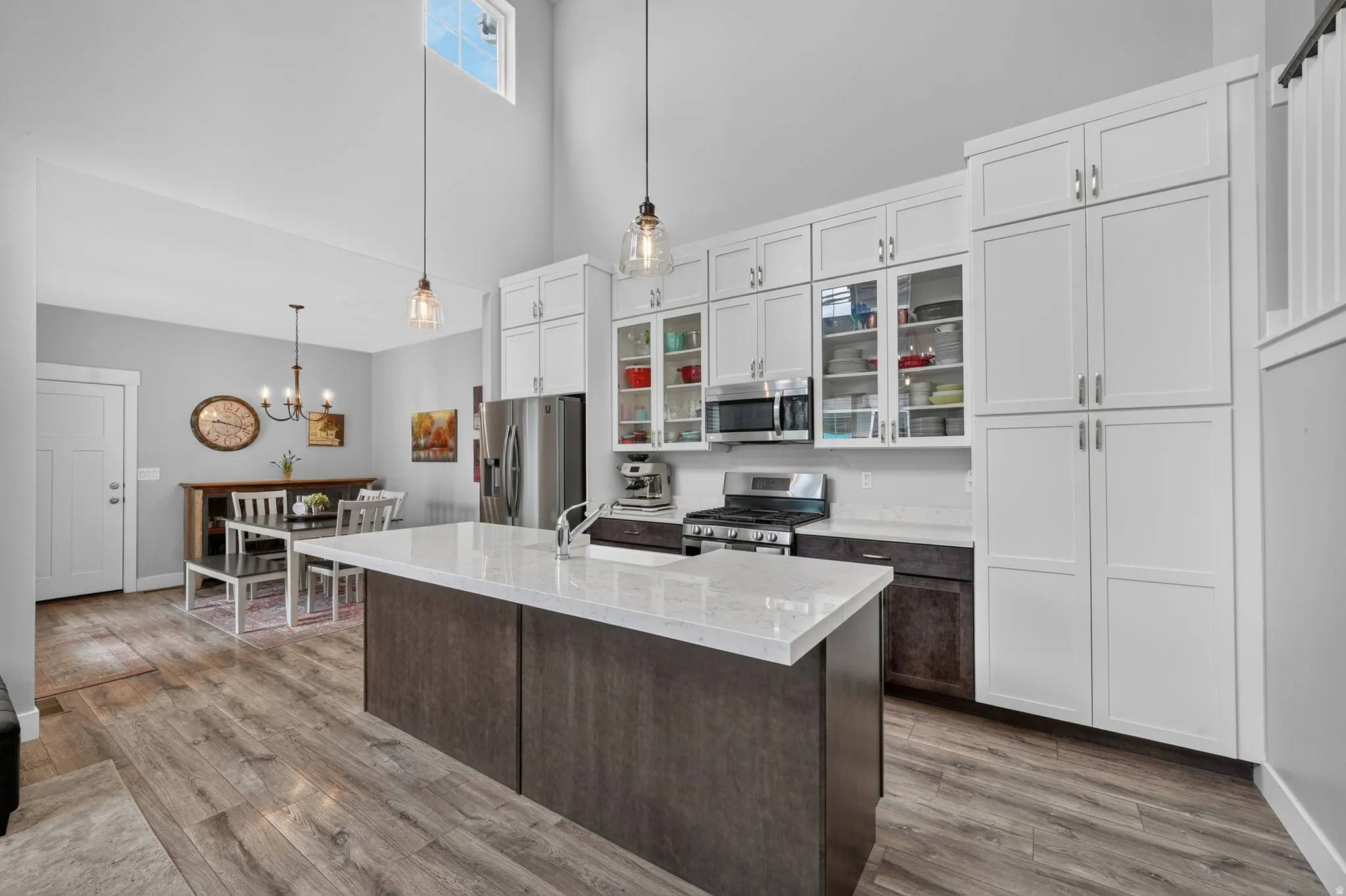 Spacious kitchen featuring an expansive island with a light-toned countertop, wood-finish flooring, and a mix of white upper cabinetry and darker lower cabinetry