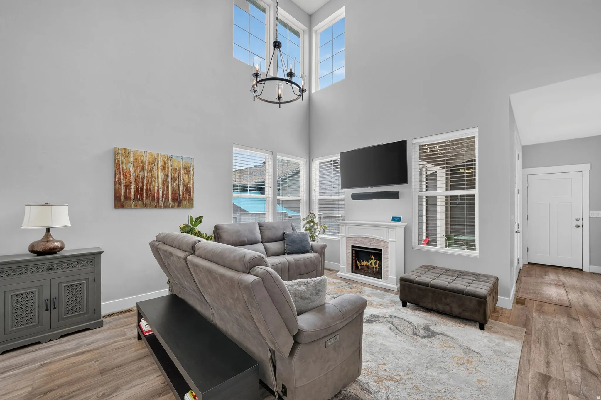 Open-concept living area with soaring ceilings, a decorative fireplace with mantel, recessed media space, wood-finish flooring, and multiple large windows