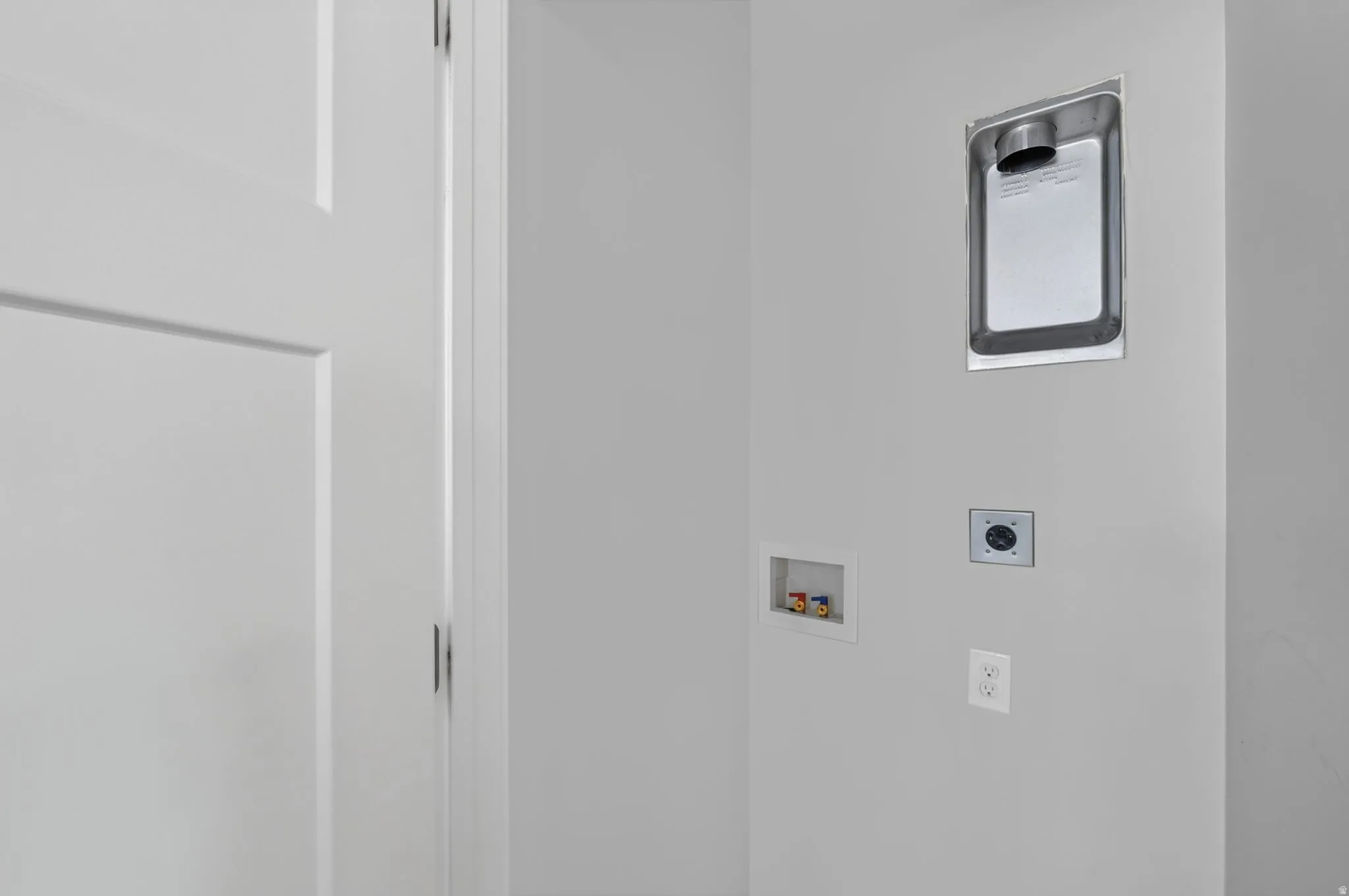 Dedicated laundry area featuring a dryer vent recess, washer hookups, and an electrical outlet, complemented by a white paneled door