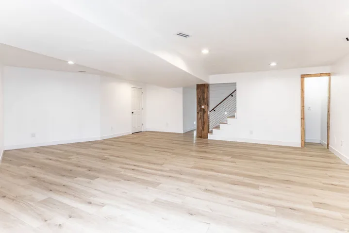 Expansive open-concept  basement room featuring light wood-finish flooring and recessed lighting