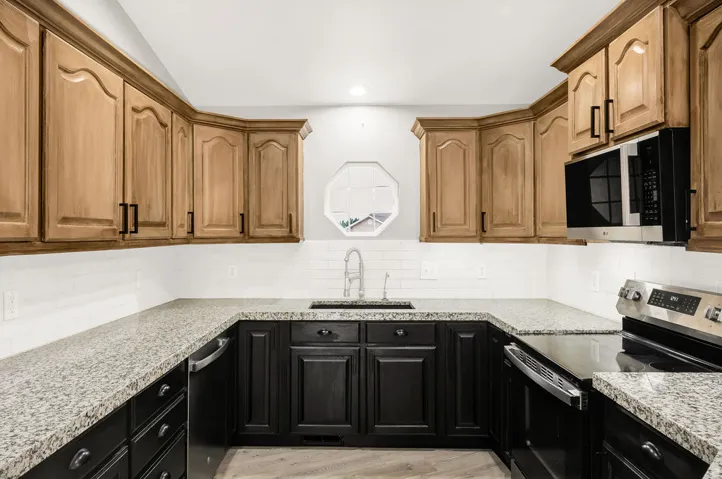 U-shaped kitchen featuring two-tone cabinetry, stone-finish countertops, subway tile backsplash, and stainless steel appliances