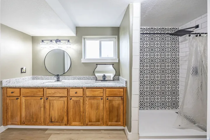 Dual sink vanity featuring a granite-style countertop, natural wood-finish cabinetry, and matte black fixtures