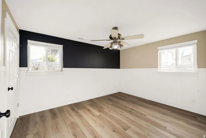 Room featuring wood-finish flooring, white beadboard wainscoting, and a ceiling fan with integrated lighting