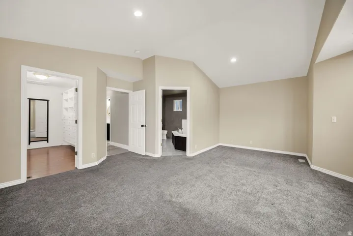 Spacious room featuring vaulted ceilings, recessed lighting, neutral wall paint, and gray carpet flooring