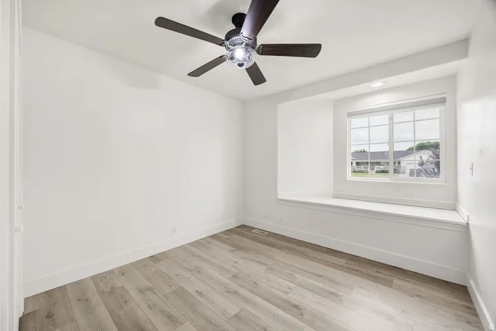 Spacious room featuring wood-finish flooring, a contemporary ceiling fan, and a built-in window seat