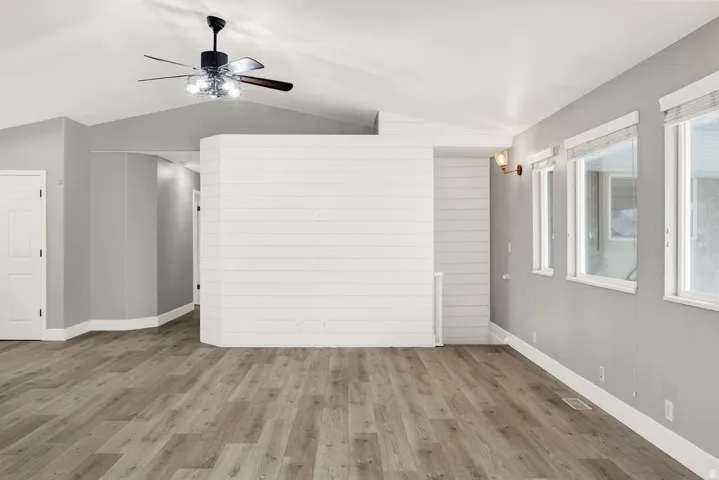 Open-concept living space featuring wood-finish flooring, a contemporary ceiling fan with integrated lighting, and multiple windows with blinds