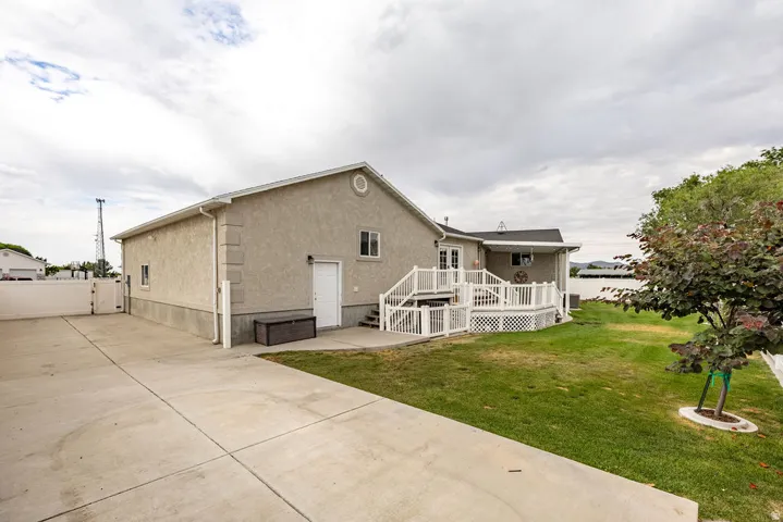 Expansive concrete driveway leading to a stucco-sided residence featuring a two-level outdoor deck with white railings