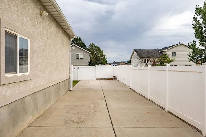 Concrete side path featuring a white vinyl fence and stucco exterior