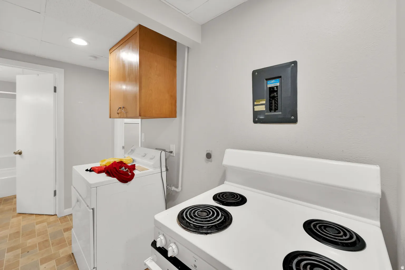Utility area featuring a freestanding range, laundry appliances, wood cabinetry, and a ceiling-mounted light fixture
