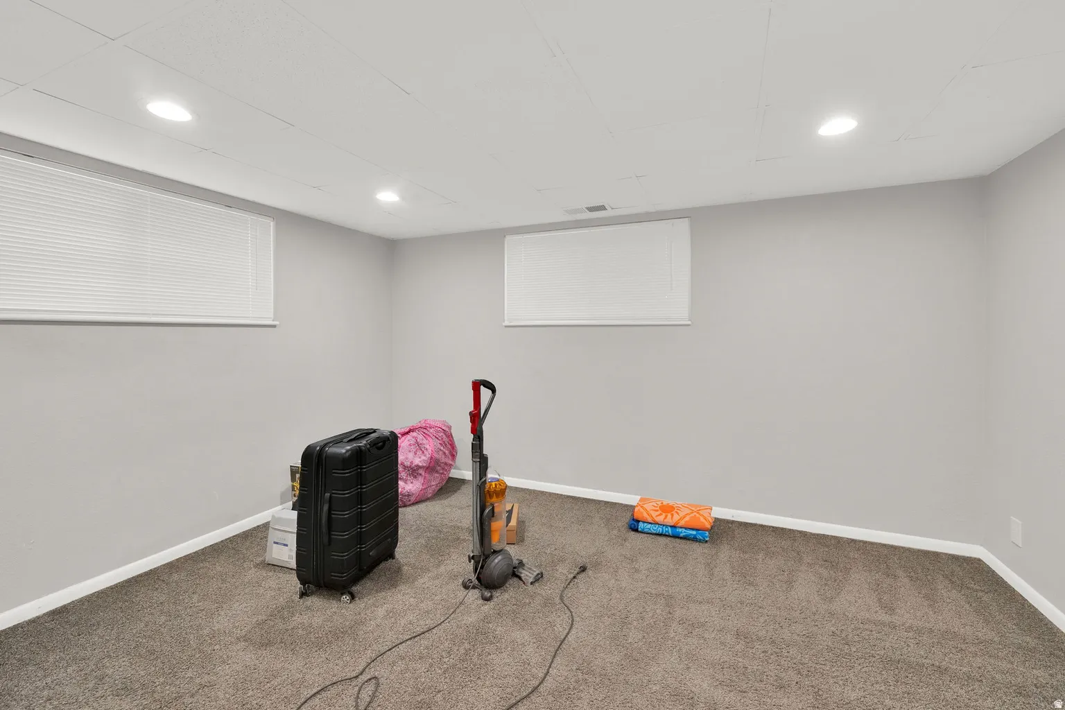 Finished room with neutral gray walls, recessed lighting, and two windows with blinds