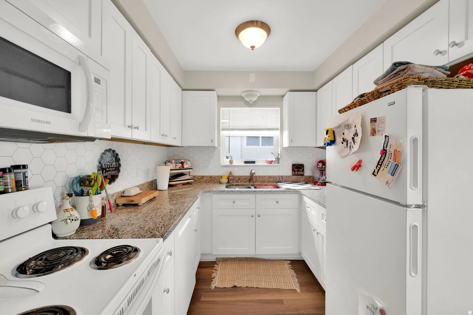 Kitchen featuring white cabinetry, wood-finish flooring, a white electric range, a white microwave, and granite-look countertops with a hexagonal tile backsplash