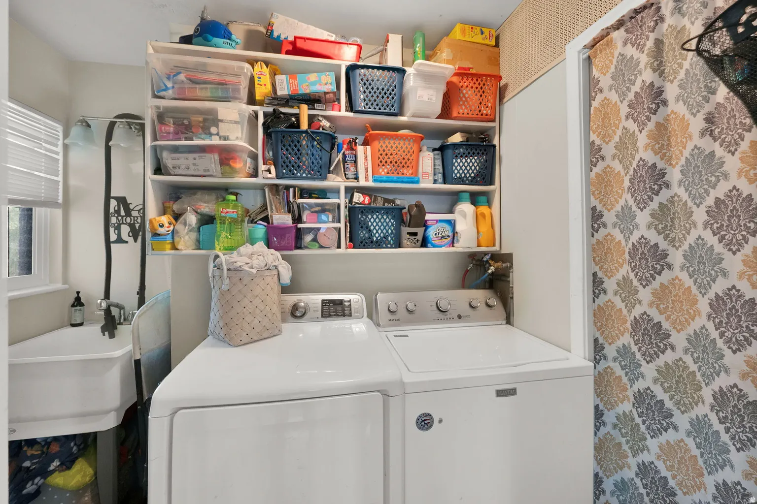 Dedicated laundry area featuring a utility sink, large overhead shelving, and window with blinds