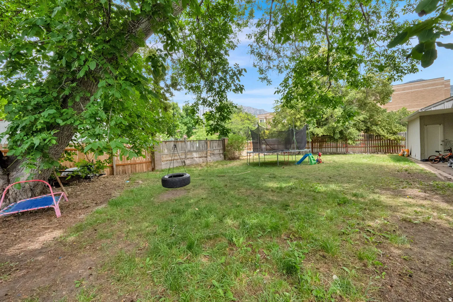 Expansive backyard featuring mature trees, a wooden fence, and a side building with an exterior door