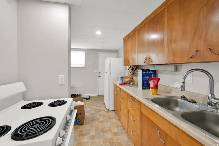 Functional kitchen featuring a white electric range, wood cabinetry, light-toned countertops, and a double basin stainless steel sink with a gooseneck faucet
