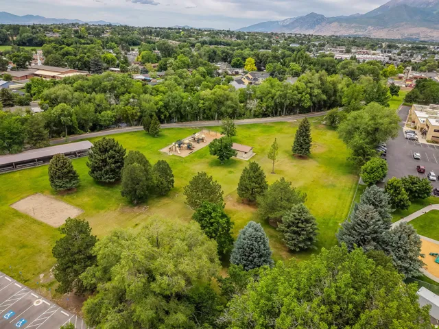 Expansive green space featuring a playground, sand volleyball court, mature trees, and covered picnic structures