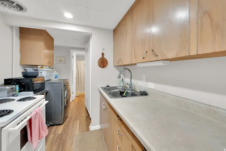 Compact kitchen area featuring wood-finish cabinetry, a double basin stainless steel sink with a chrome faucet, and solid surface countertops