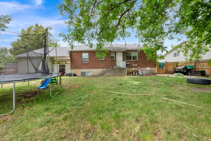 Expansive rear yard featuring green lawn space, mature tree cover, a partial privacy fence, and a brick exterior with basement windows