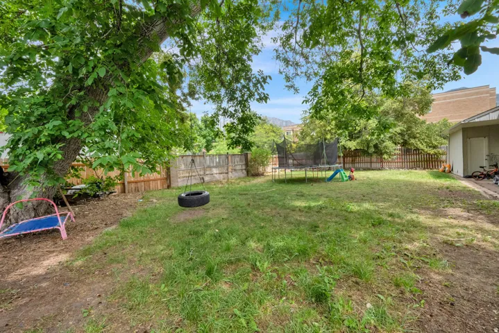 Expansive backyard featuring mature trees, a wooden fence, and a side building with an exterior door