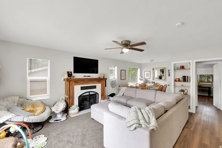 Spacious living area featuring a fireplace with a wood mantle, ceiling fan, and carpet flooring