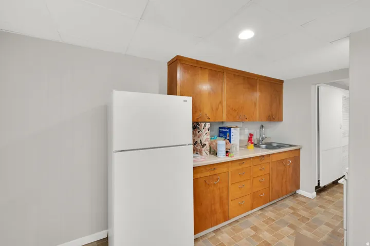 Kitchenette featuring wood-finish cabinetry, a stainless steel sink with a chrome faucet, and resilient flooring