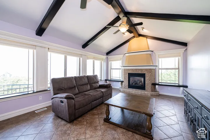 Vaulted ceilings with exposed beams, a stone-surround fireplace, and a full wall of windows define this living area