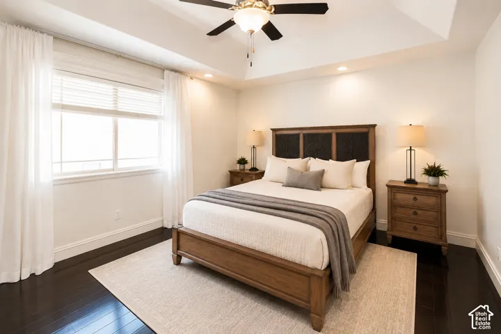 Tray ceiling with a ceiling fan and recessed lighting, large window with blinds and sheer curtains, dark wood-finish flooring, and white baseboards