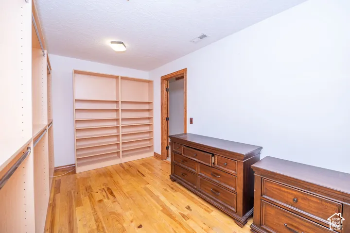 Walk-in closet featuring extensive built-in shelving, hanging rods, and wood-finish flooring