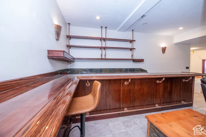 Custom built-in bar featuring rich wood finishes, open shelving, integrated stemware storage, decorative wall sconces, and a tiled backsplash