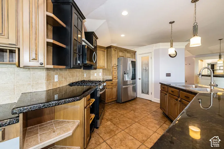 Kitchen featuring dark granite countertops with a chiseled edge, a tile backsplash, stainless steel appliances, and two-tone cabinetry with glass-front uppers