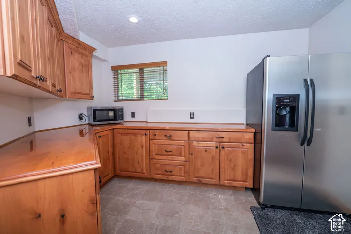Level 3 kitchenette Light wood cabinetry with dark hardware, a stainless steel refrigerator, and wood-finish countertops