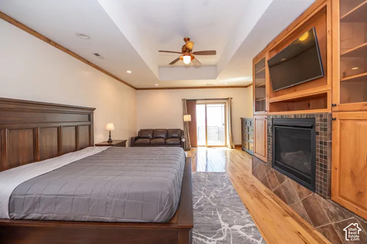 Spacious Master Bedroom featuring wood-finish flooring, a built-in entertainment center with an electric fireplace, a tray ceiling with a ceiling fan, and recessed lighting