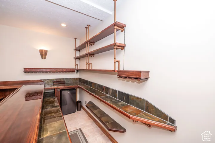 Built-in bar featuring wood-finish countertops, natural stone tile backsplash, industrial-style pipe shelving, recessed lighting, and an under-counter beverage refrigerator