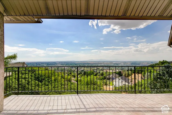 Spacious outdoor balcony with a tile surface, black metal railing, and a distant cityscape