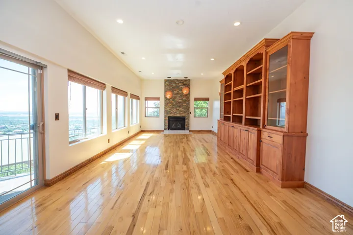Spacious interior featuring wood-finish flooring, a stone-clad fireplace with sconce lighting, built-in wooden cabinetry, recessed lighting, and a sliding glass door leading to a balcony. 10 ft. ceilings.