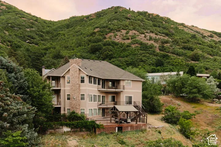 Multi-level residence featuring a neutral-toned exterior, stone accent chimney, multiple balconies, an expansive wood deck, and an integrated gazebo