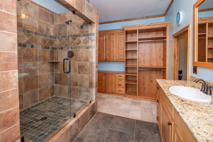 Tile shower enclosure with a glass door, custom wood cabinetry, granite-finish countertop with an undermount sink, and integrated shelving