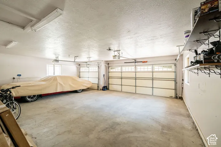 Spacious three-car garage featuring multiple garage doors, concrete flooring, and built-in wall shelving