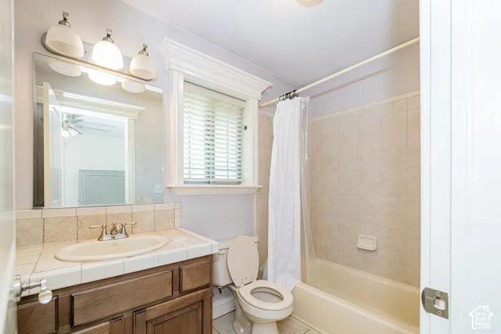 Bathroom featuring a single vanity with wood-finish cabinetry, a tiled countertop, and an undermount sink