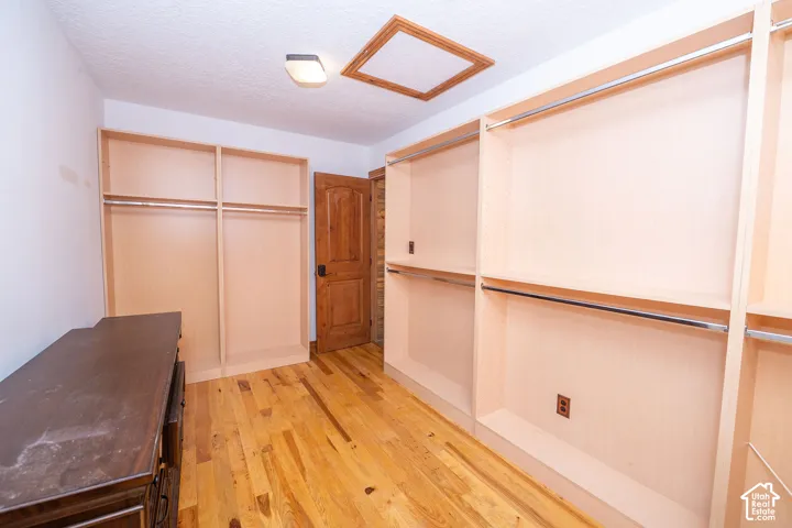 Custom walk in closet featuring wood-finish flooring, built-in shelving, hanging rods, an integrated ceiling light fixture, and a wood-panel door entering the wine cellar room.