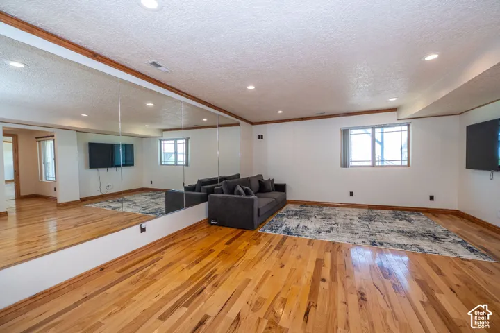 Expansive Fitness room featuring wood-finish flooring, a full-length mirrored wall, a window with horizontal blinds, recessed lighting, and a textured ceiling.