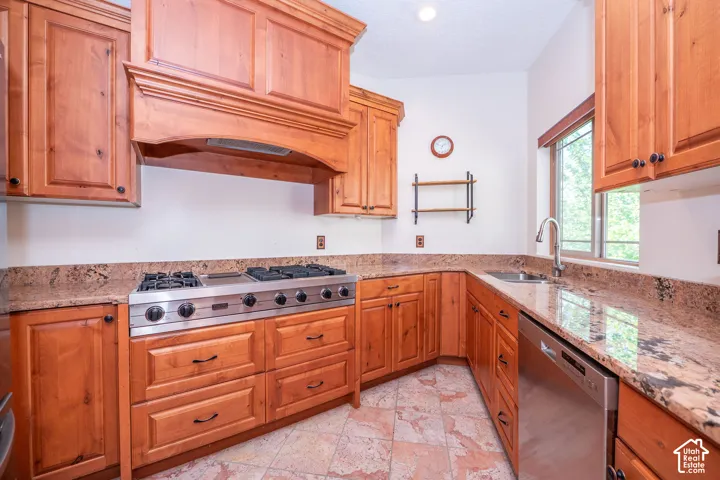 Second Level Kitchen featuring abundant wood cabinetry, patterned stone countertops, stainless steel gas range, stainless steel dishwasher, and a stainless steel sink with a gooseneck faucet