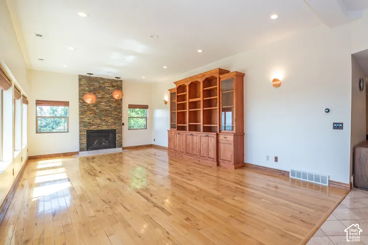 Spacious room featuring wood-finish flooring, a stacked stone fireplace with a white hearth, and wall of multiple windows and nightly west facing sunset views.
