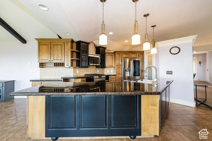 Kitchen featuring a central island with a dark countertop and paneled base, stainless steel appliances, and a mix of light and dark wood-finish cabinetry