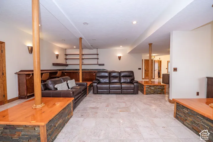 Spacious entertainment area featuring a built-in bar with wood cabinetry and shelving, stone veneer accents, recessed lighting, and tile flooring