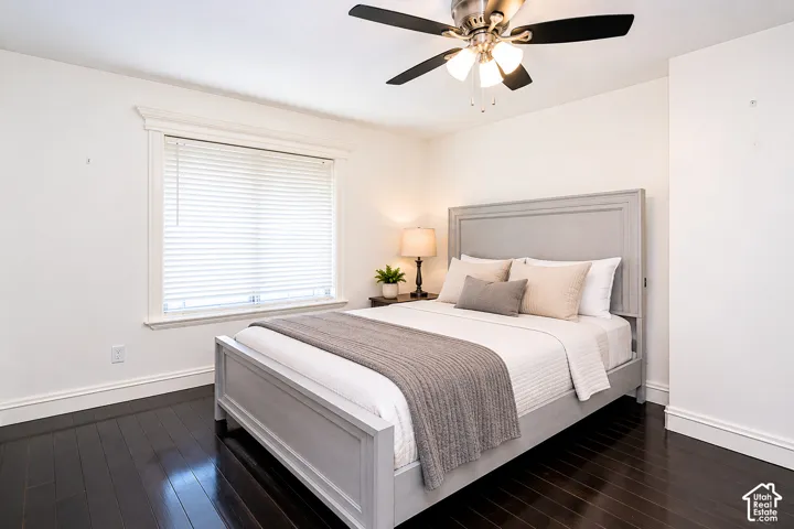 Spacious room featuring dark wood-finish flooring, white baseboards, and a window with white blinds. Bedroom includes an ensuite.